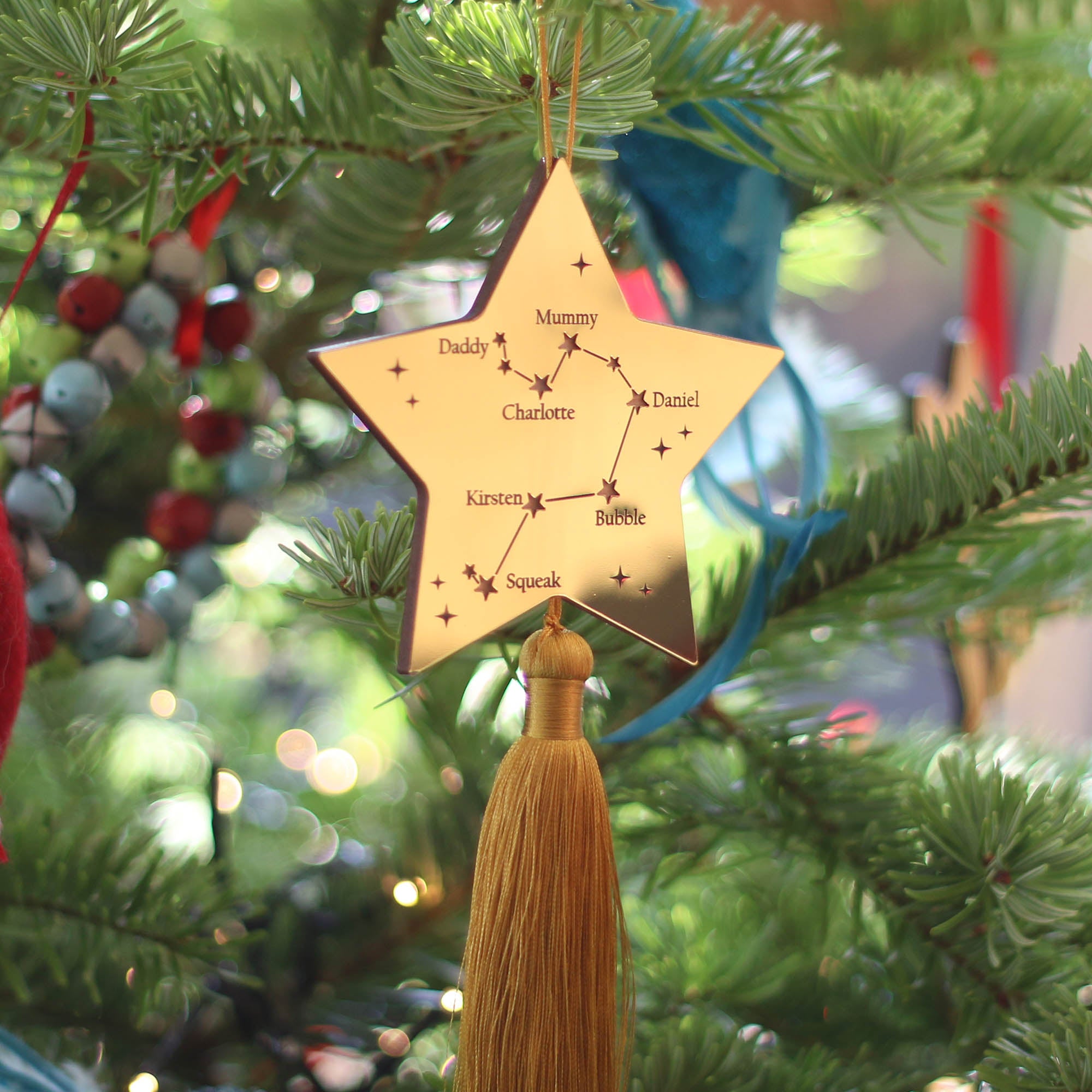 Gold star-shaped ornament with tassel against a dark blue background with blurred lights