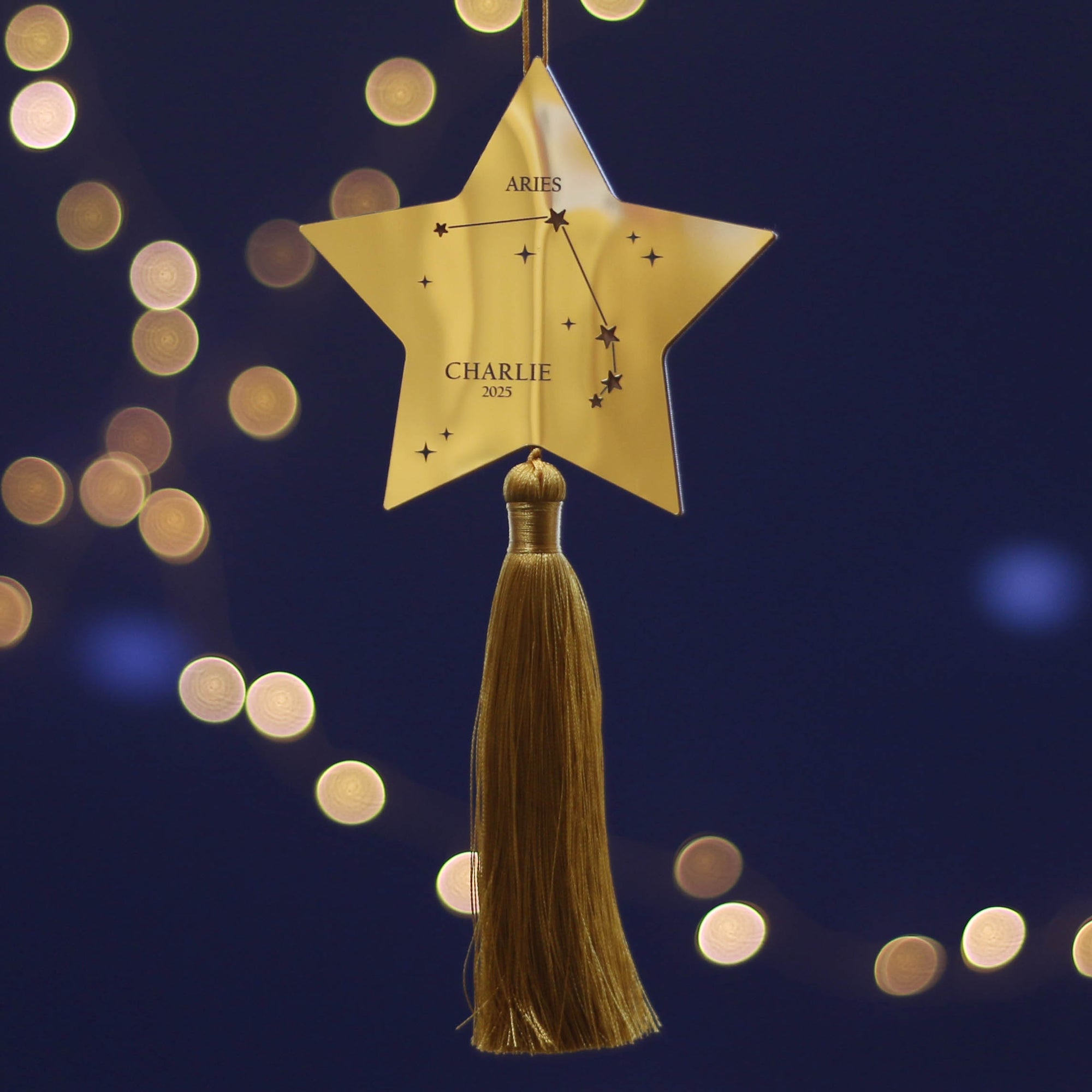 Gold star-shaped ornament with tassel against a dark blue background with bokeh lights