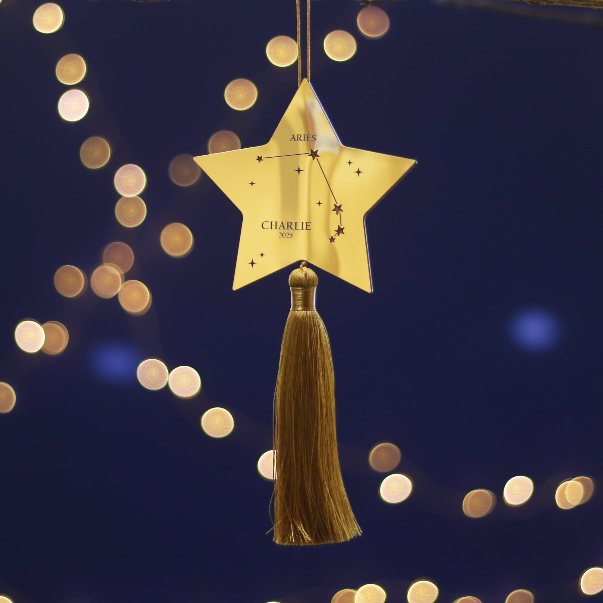 Gold star-shaped ornament with tassel against a dark blue background with bokeh lights