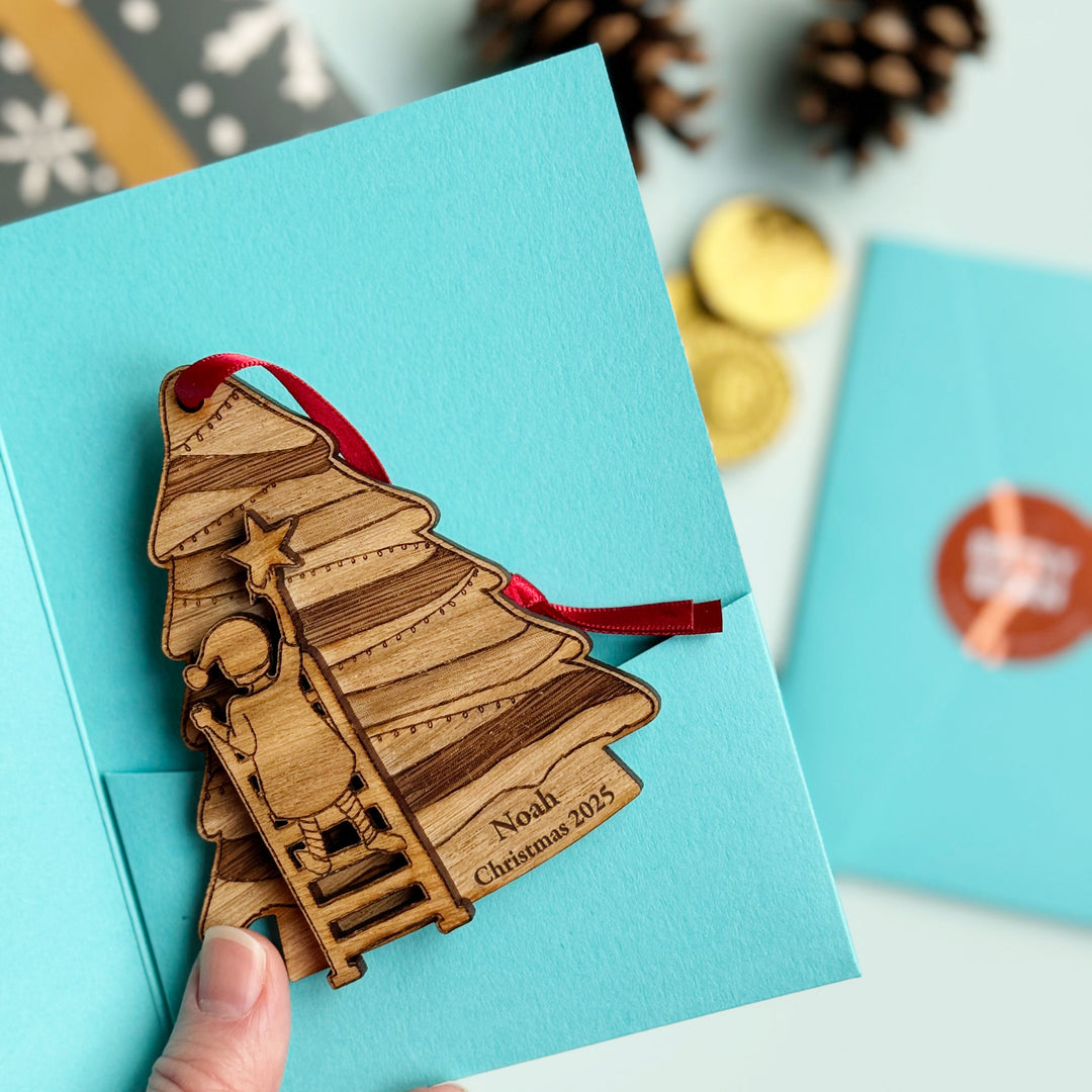 Custom engraved festive bauble with child decorating the tree, blue gift sleeve background.