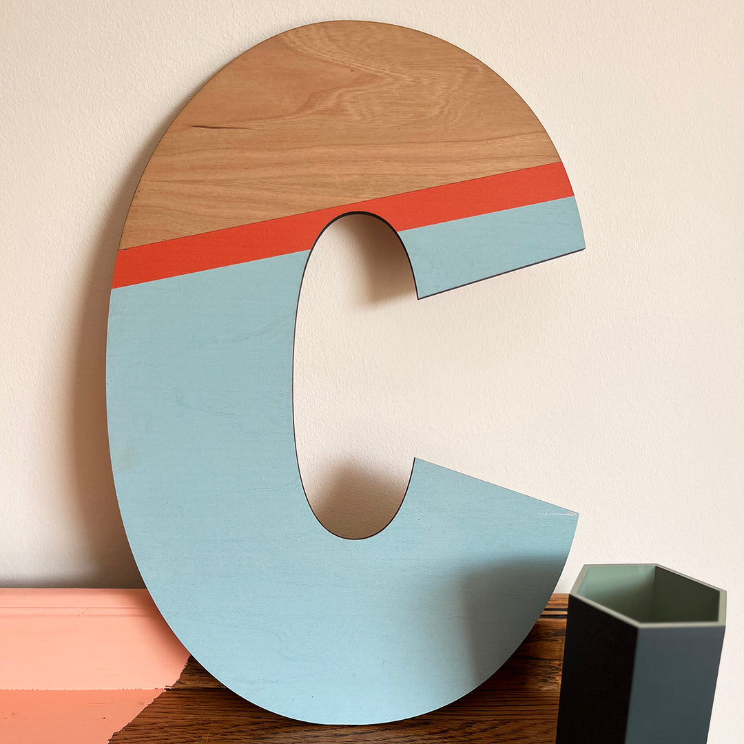 Large wooden letter "C" painted in a vibrant color scheme, with a combination of natural wood, blue, and red.