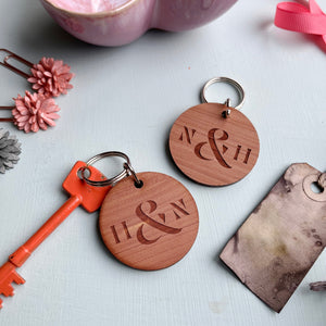 Pair of circular wooden keyrings engraved with initials and an ampersand