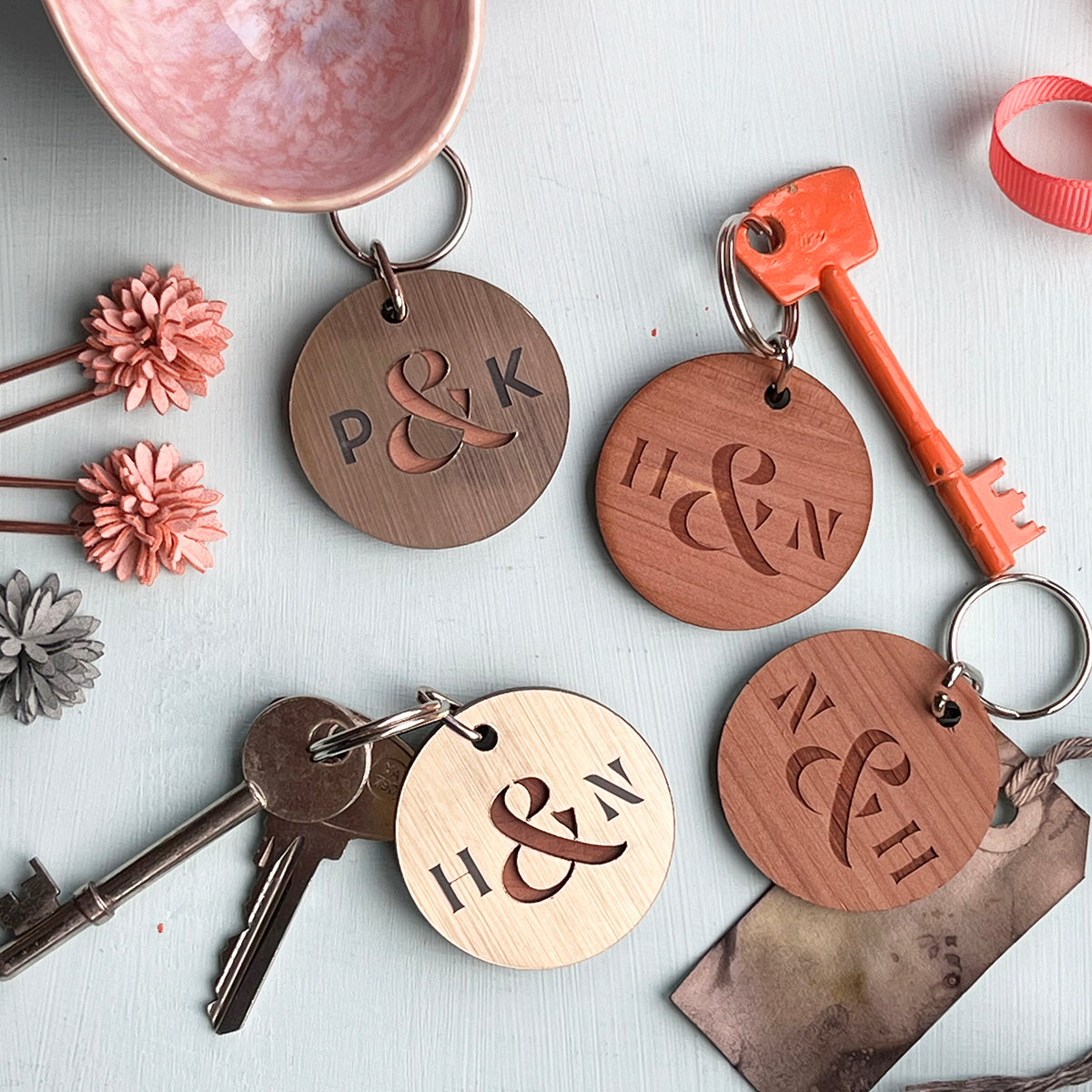 Selection of wooden and metallic circular keyrings engraved with initials and an ampersand