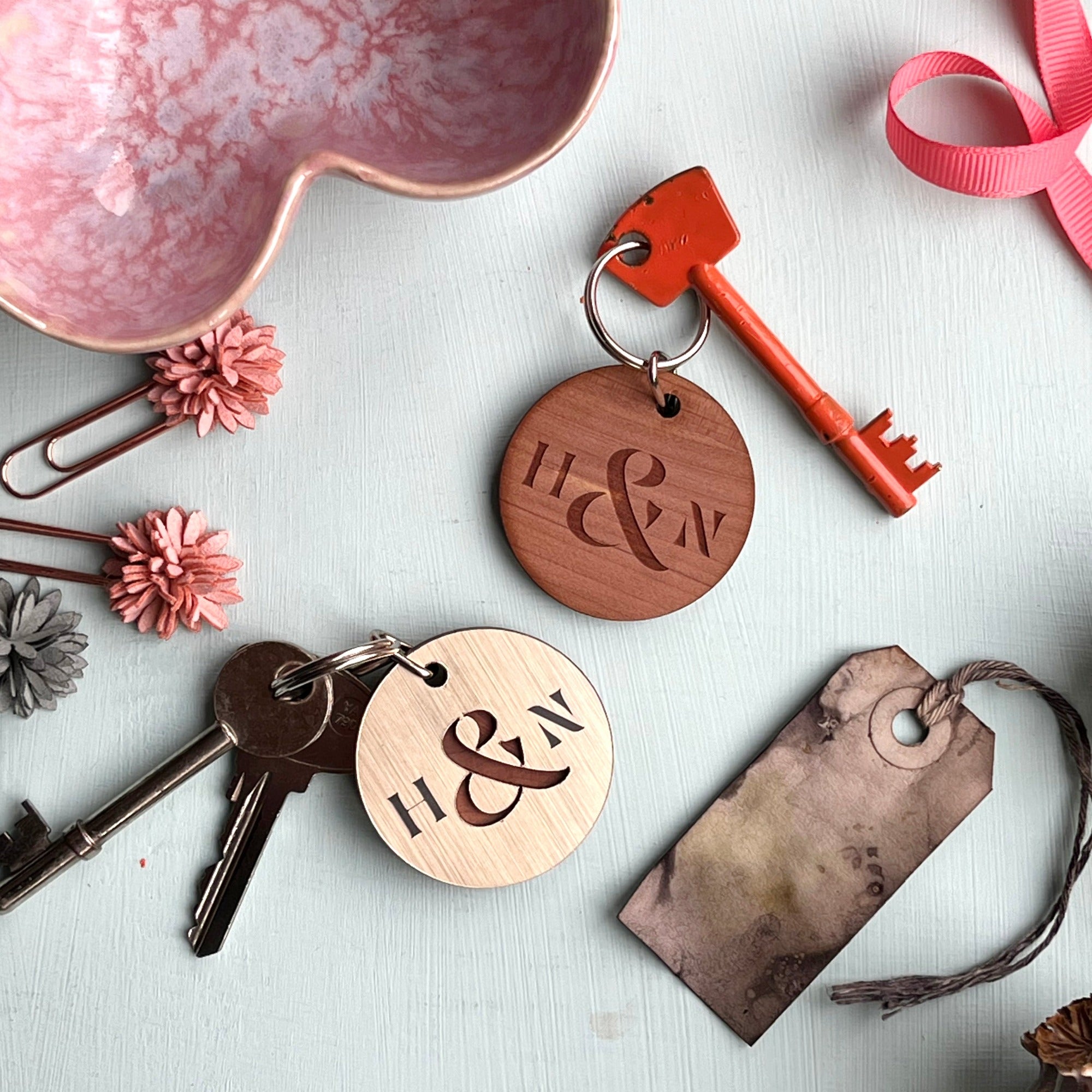 Pair of circular keyrings, 1 made from wood and 1 with a metallic gold finish, engraved with initials and an ampersand