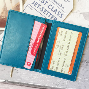 The leather cardholder minimalist wallet is lying open on a grey table. The interior shows a clear plastic window on one side where a photo or ID card can be displayed. On the other side, there are two credit card slots to hold cards, travel tickets, or a folded emergency banknote.