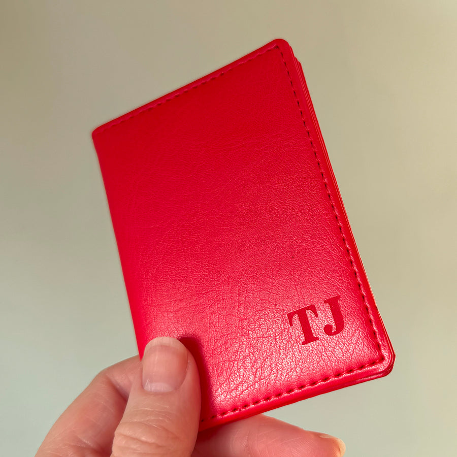 Close-up of a hand holding a red leather wallet with custom initials, displayed against a soft neutral background. Women's card holder, compact and perfect for travel lovers gift. 
