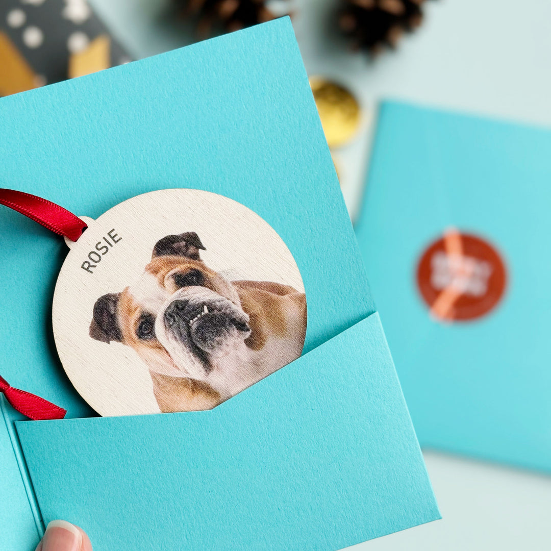 Engraved wooden Christmas dog ornament with name and red ribbon hanger in a blue gift sleeve 