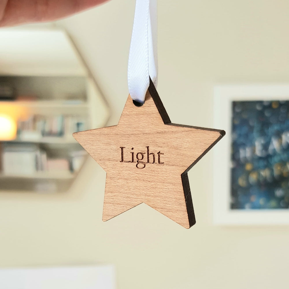 Wooden star ornament engraved with the word "Light," hanging from a white ribbon.