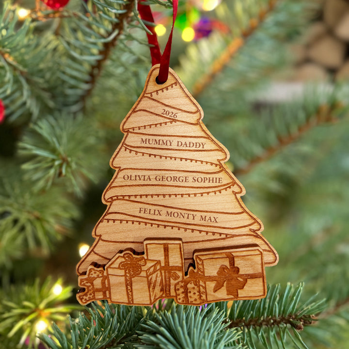 Wooden engraved Christmas tree ornament with multiple spaces for personalised family names, and protruding wooden presents at the bottom, hung on a Christmas tree.