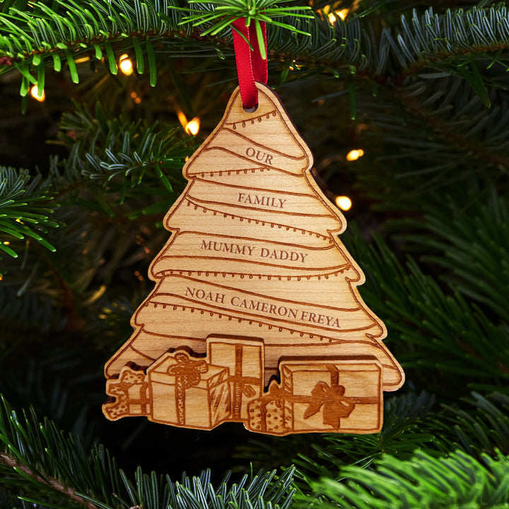 Wooden engraved Christmas tree ornament with multiple spaces for personalised family names, and protruding wooden presents at the bottom, hung on a Christmas tree.