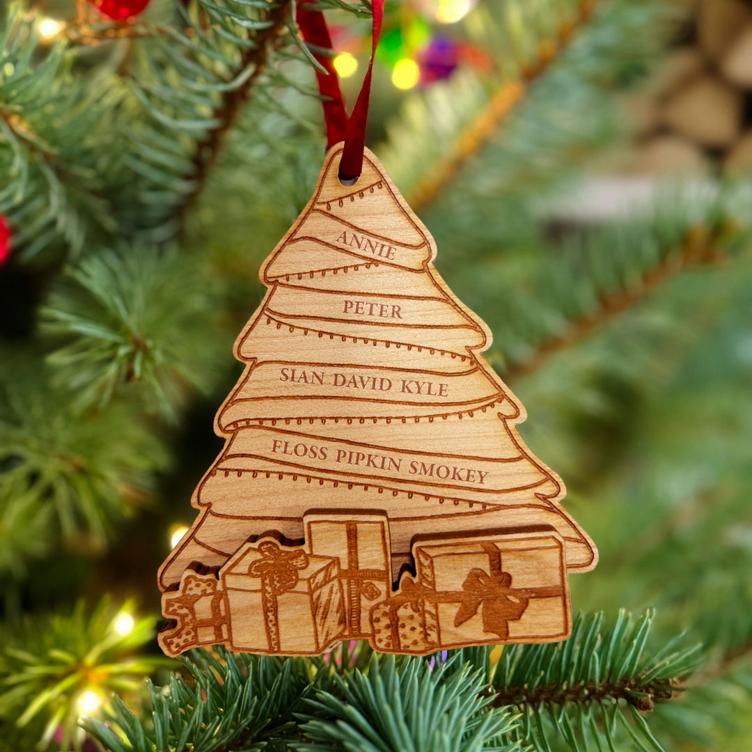 Wooden engraved Christmas tree ornament with multiple spaces for personalised family names, and protruding wooden presents at the bottom, hung on a Christmas tree.