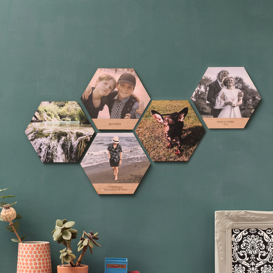 A set of five hexagon-shaped wooden photo tiles displayed on a wall, each with a different personal photo printed on them, arranged in a scattered pattern with personalised text option available. Perfect unique photo collage wall art prints.