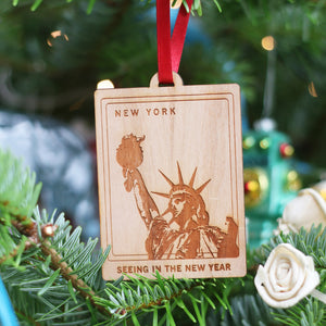 Sustainable cherry veneer wood Christmas tree personalised bauble decoration ornament with Statue of Liberty New York travel memory gift engraved design hanging on a Christmas tree with a red ribbon. Perfect gift for adventurers or hang your favourite van life destination on the van mirror!