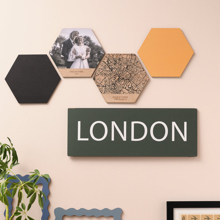 A wooden vibrant wall sign with the word 'LONDON' printed in large white letters, evoking a travel destination displayed on a wall alongside other decorative items.