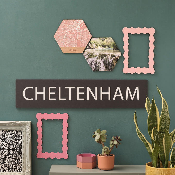 Custom hexagon wall arts above a destination bus blind style Cheltenham location favourite place wall art gift, a stylish way to enhance your home with a personal touch to commemorate a travel memory. On a forest green wall adorned with picture frames and plants.