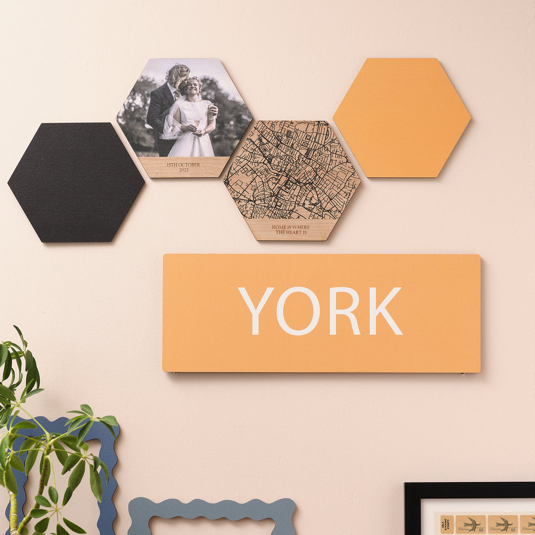 Small size wooden vibrant yellow wall print of York city break travel destination with hexagonal wall prints above and frames and plants below.