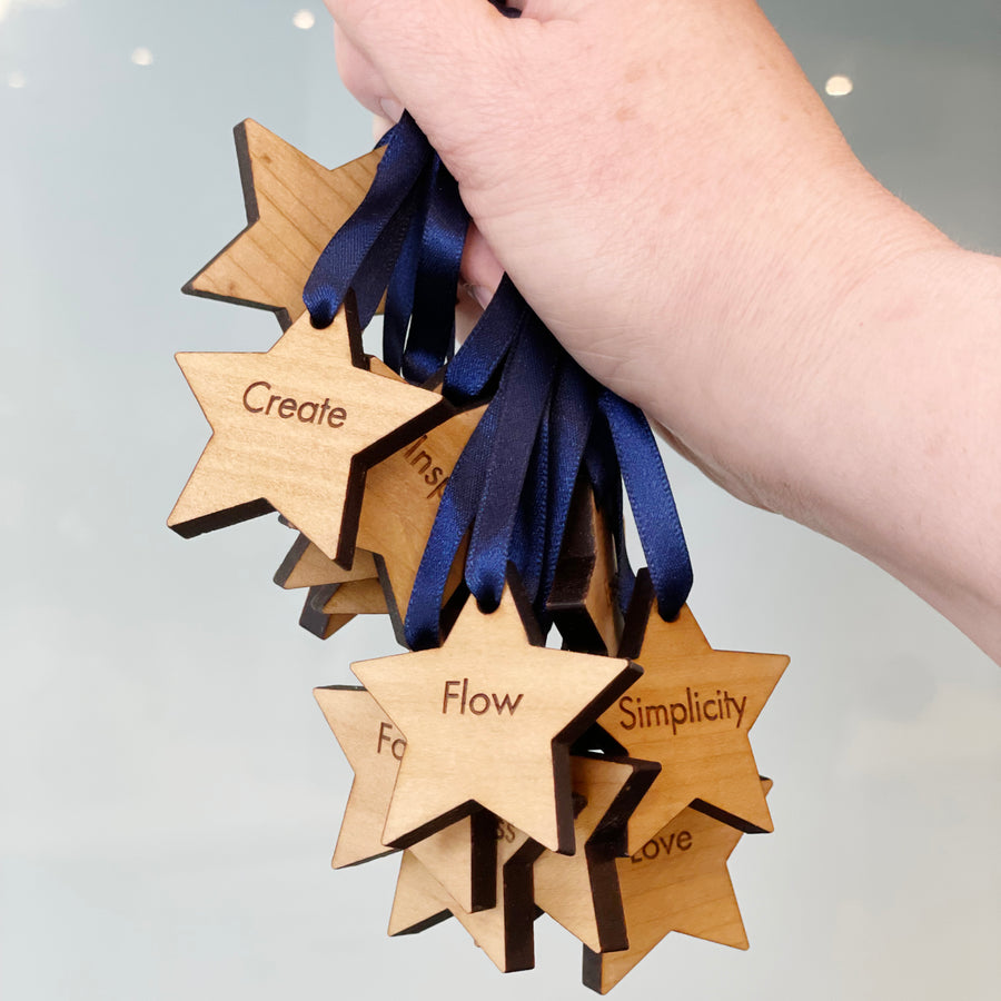 Hand holding wooden star-shaped ornaments with engraved words and navy blue ribbons.