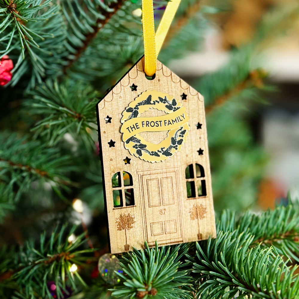 Wooden house Christmas bauble with personalised golden wreath and engraved details on a Christmas tree.