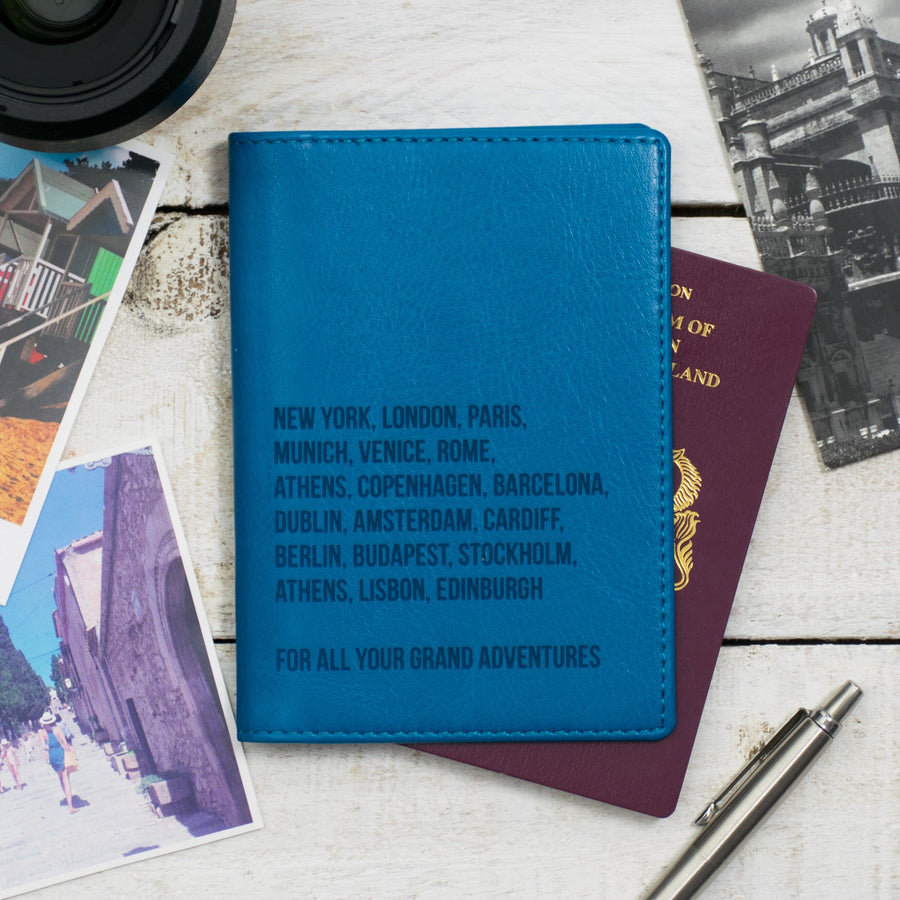 Turquoise blue travel wallet with embossed city names, surrounded by travel essentials like a passport, boarding passes, and postcards.