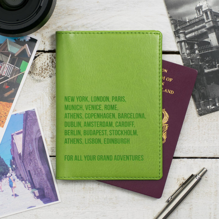 Personalized green leather passport holder featuring a list of famous cities, placed on a wooden table with travel documents and a pen.