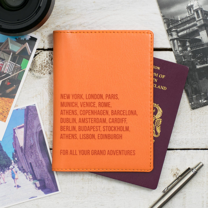 A stylish orange travel wallet engraved with city names, next to a passport and travel memorabilia.