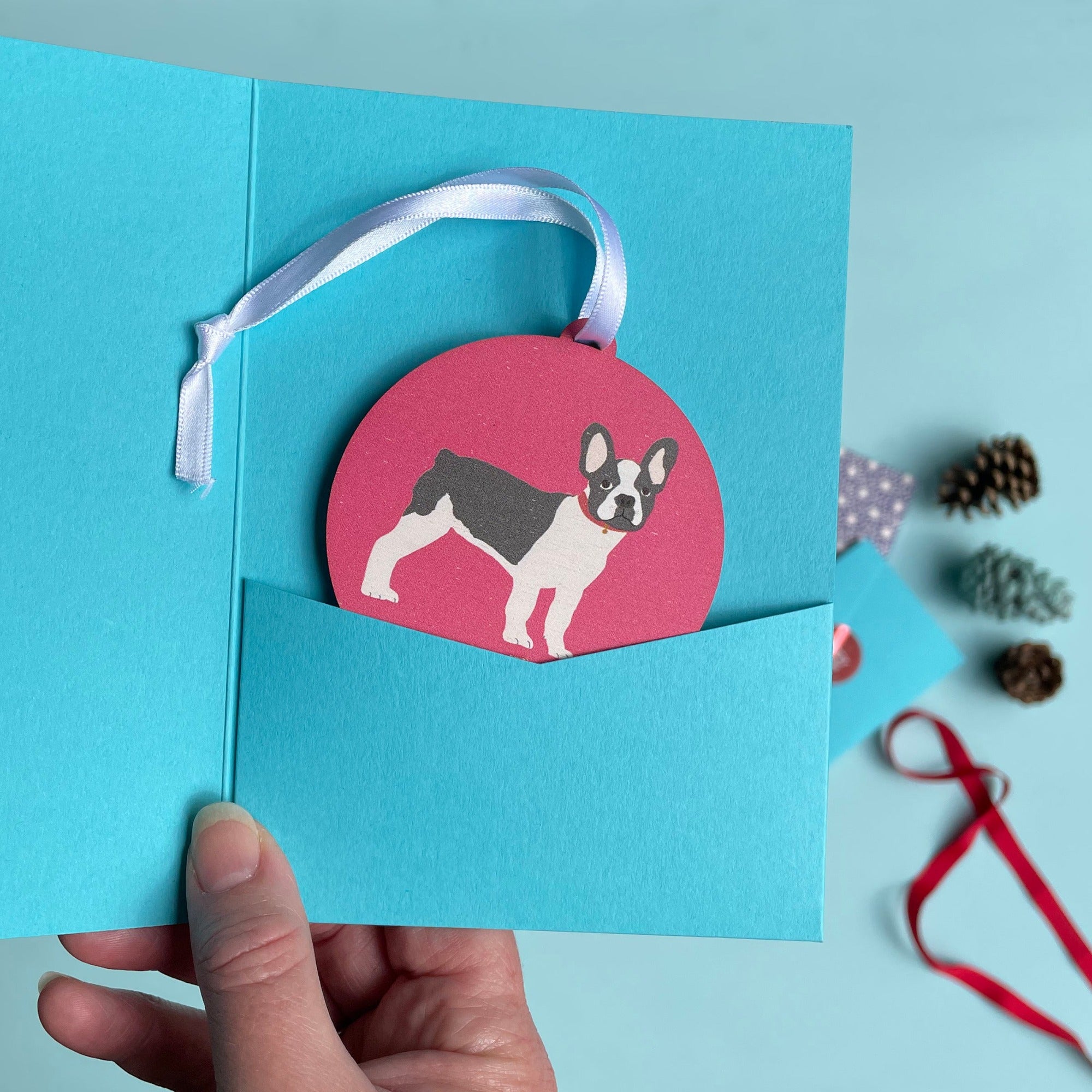 Painted wooden decoration of a french bulldog dog on a coloured background in a turquoise gift sleeve