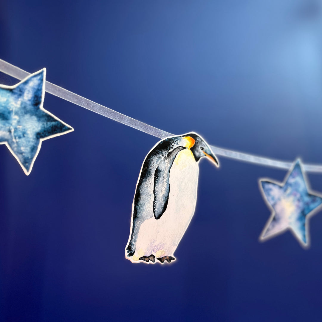 A penguin-themed garland with blue stars and penguins hanging on a blue background.