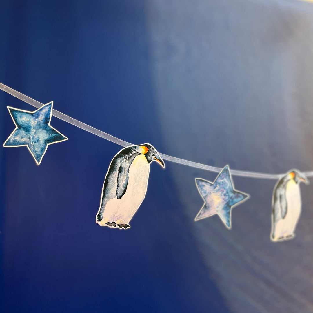 A penguin-themed garland with blue stars and penguins hanging on a blue background.