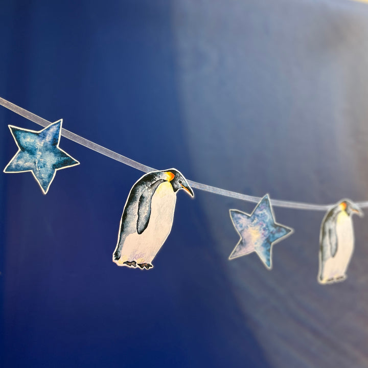 A penguin-themed garland with blue stars and penguins hanging on a blue background.