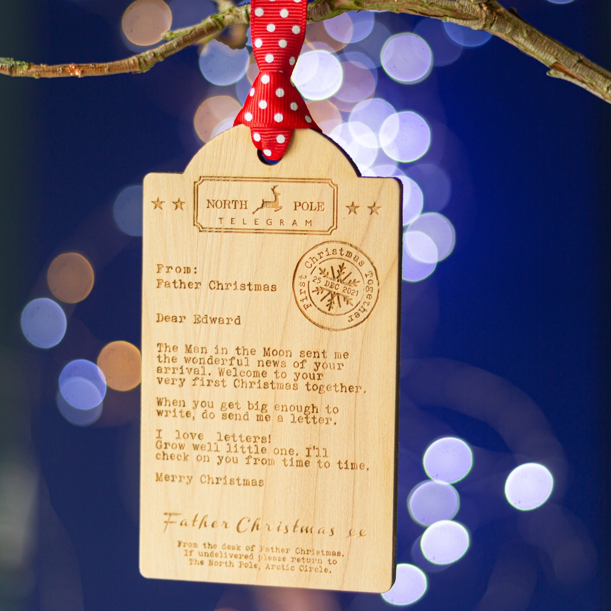 Wooden telegram shaped decoration with a message from Father Christmas to an adopted child to celebrate their first Christmas in their family. Hanging with a red spotty ribbon