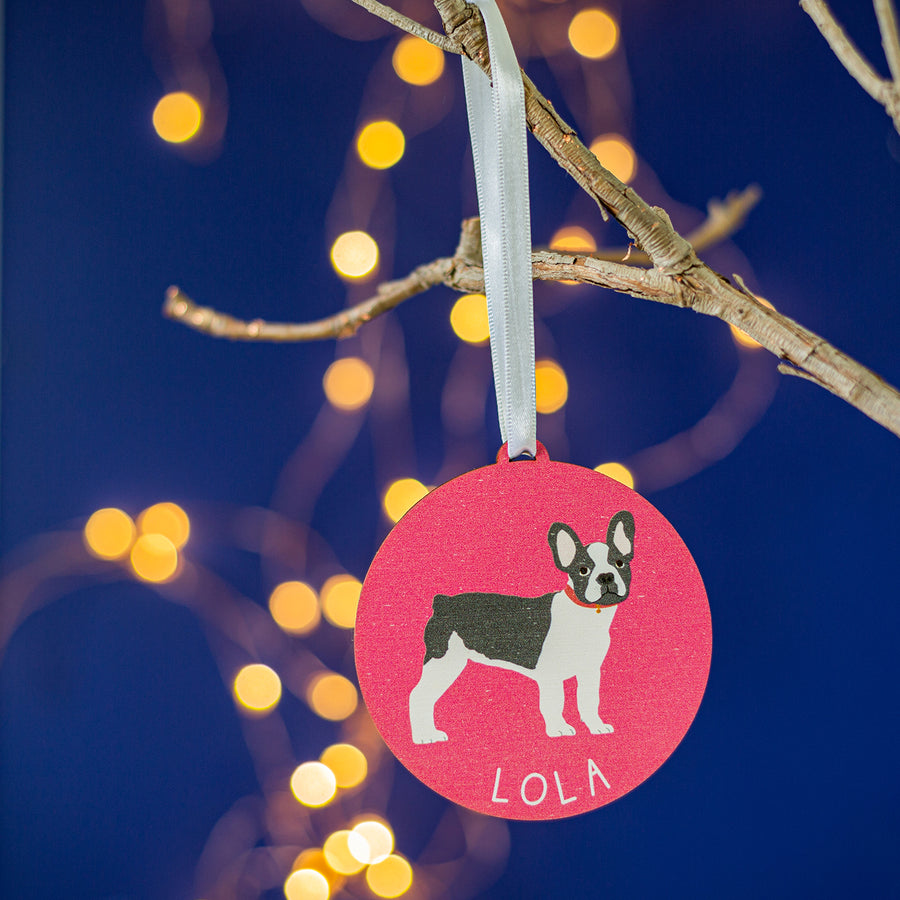 A personalised Christmas tree decoration featuring an illustration of a French Bulldog on a red background, with the name 'LOLA' printed at the bottom.