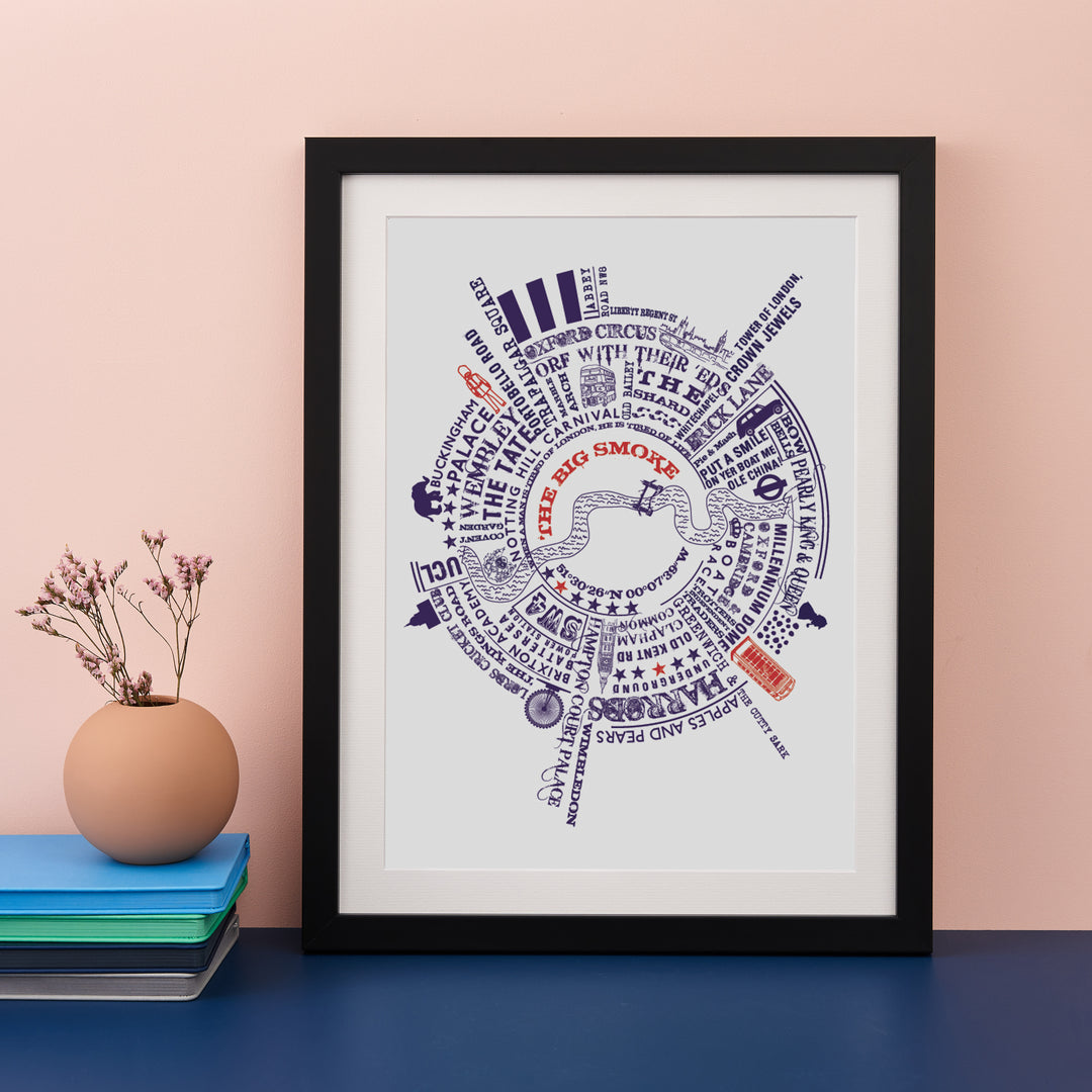 A framed circular map print of London landmarks and phrases hangs on a wall above a dark console table. Two glass vases with flowers are on the table. The print features "THE BIG SMOKE" in red and blue text.