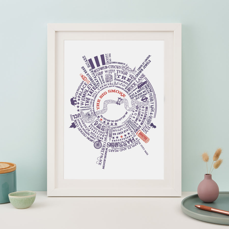 A framed print with a circular map of London landmarks and phrases, including "OXFORD CIRCUS," "THE SHARD," and "PUT A SMILE ON YER BOAT ME OLE CHINA." The print is in a white frame and sits on a table with other decorative items.