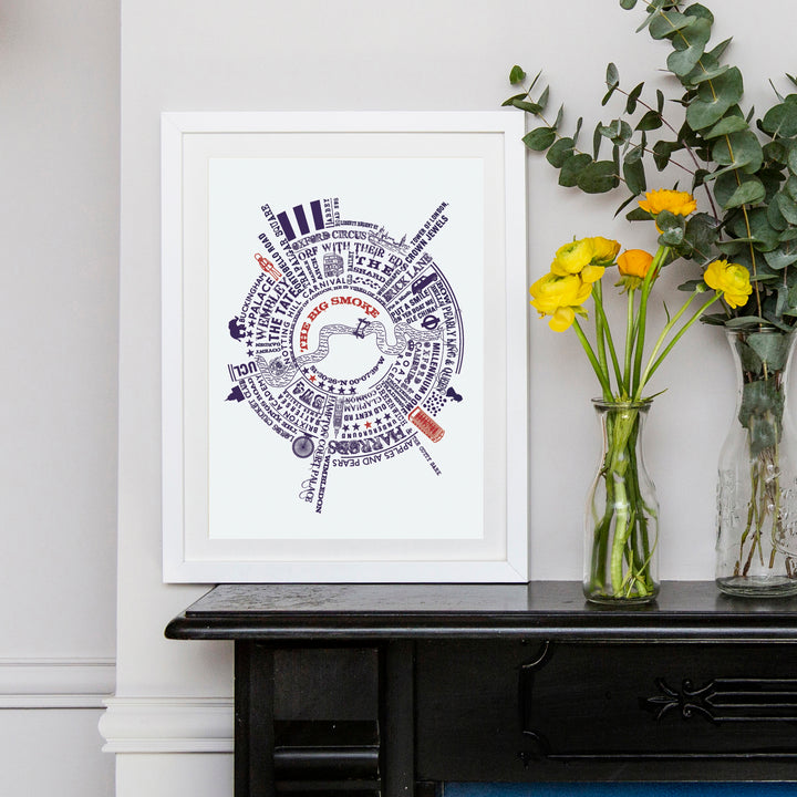 A framed circular map print of London landmarks and phrases hangs on a wall above a dark console table. Two glass vases with flowers are on the table. The print features "THE BIG SMOKE" in red and blue text.