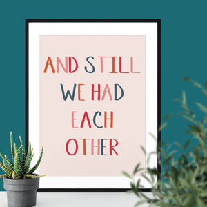 Pale pink print in a black frame printed with the text "and still we had each other" 