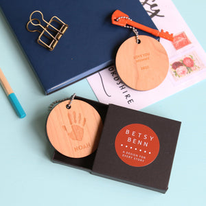 Round wooden keyring engraved with  a child's handprint and personalised text. in a black gift box