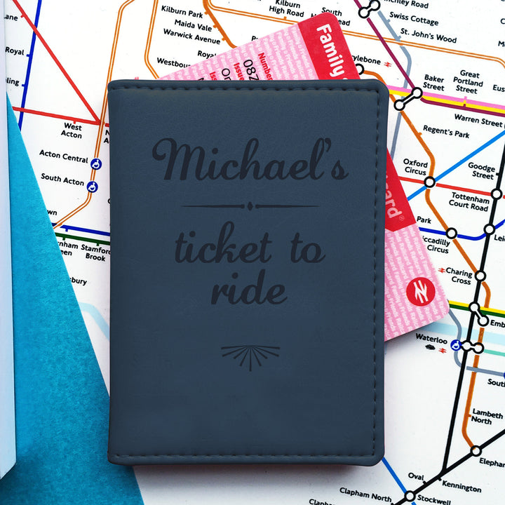  A dark blue slim card holder with "Michael's ticket to ride" engraved on the front, sits on a tube map of London. A pink "Family & Friends Railcard" protrudes from the top.