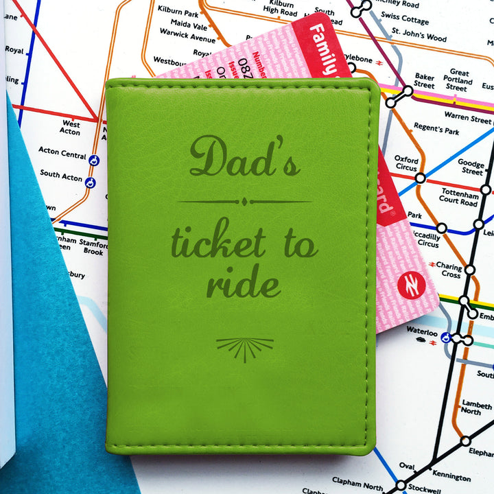 A green travel cardholder with "Dad's ticket to ride" embossed on the front lies atop a London tube map, partially revealing a pink "Family & Friends Railcard." Can also be used as a slim minimalist wallet.

