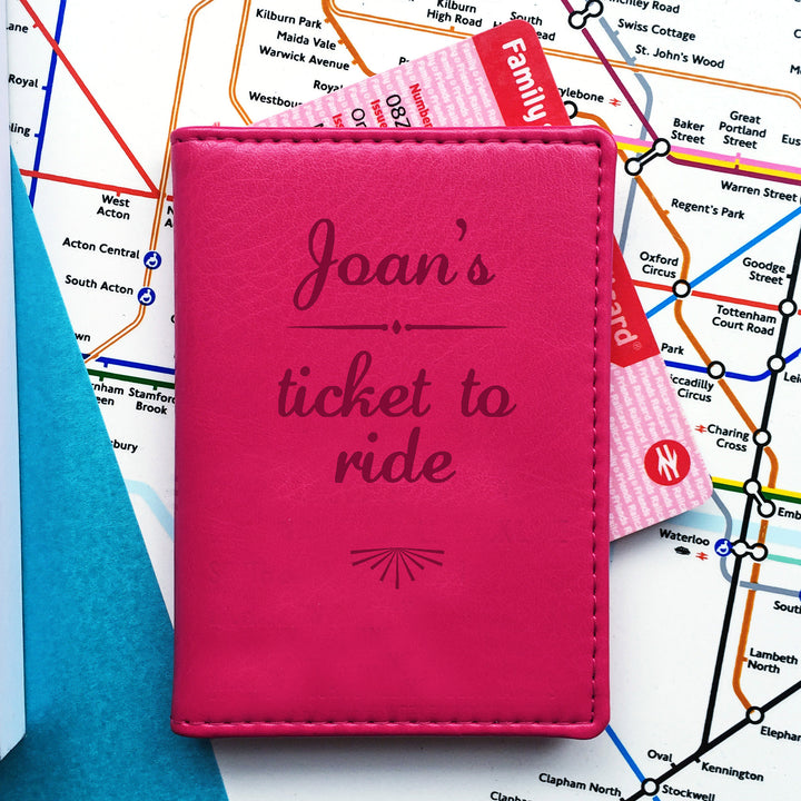 A pink card holder with "Joan's ticket to ride" engraved on the front, sits on a map of London. A pink "Family & Friends Railcard" protrudes from the top.