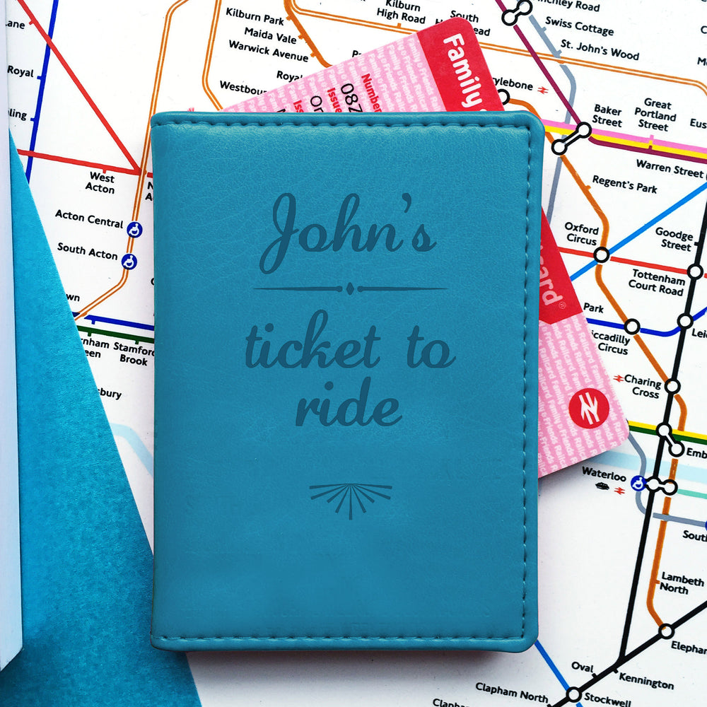 A turquoise oyster card holder with "John's ticket to ride" engraved on the front, sits on an underground map of London. A pink "Family & Friends Railcard" protrudes from the top.