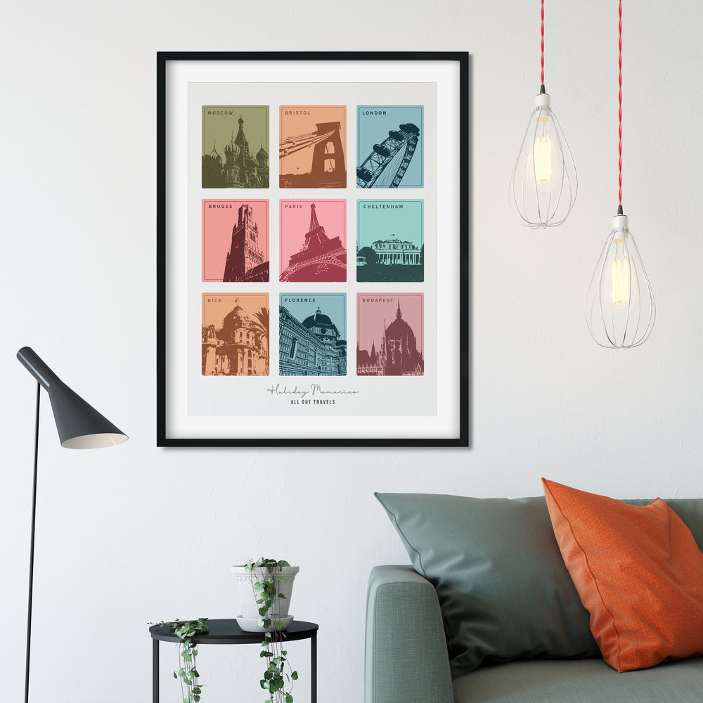 framed print with nine colorful squares, each depicting a different European city landmark, hangs above a gray couch with orange pillows. The print is personalized with "Holiday Memories" and "All Our Travels." Two pendant lights hang above the couch.