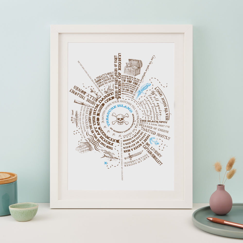 A framed print with a circular design featuring pirate quotes and illustrations is displayed on a table. Next to it are a small plant pot, a bowl, a vase with dried flowers, and a pen.
