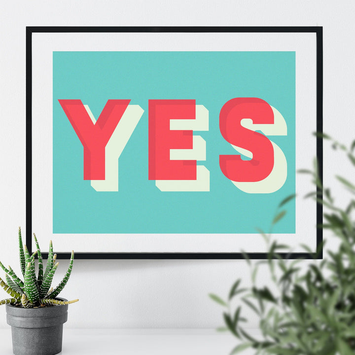 A framed art print with the word "YES" in bold, colorful typography on a turquoise background.