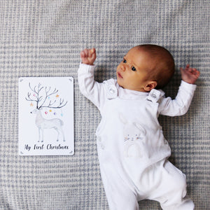 Baby lying next to a reindeer print with text saying "My First Christmas"