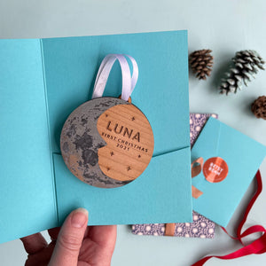 Wooden round decoration with a silver crescent  moon and personalised text. with a turquoise gift envelope
