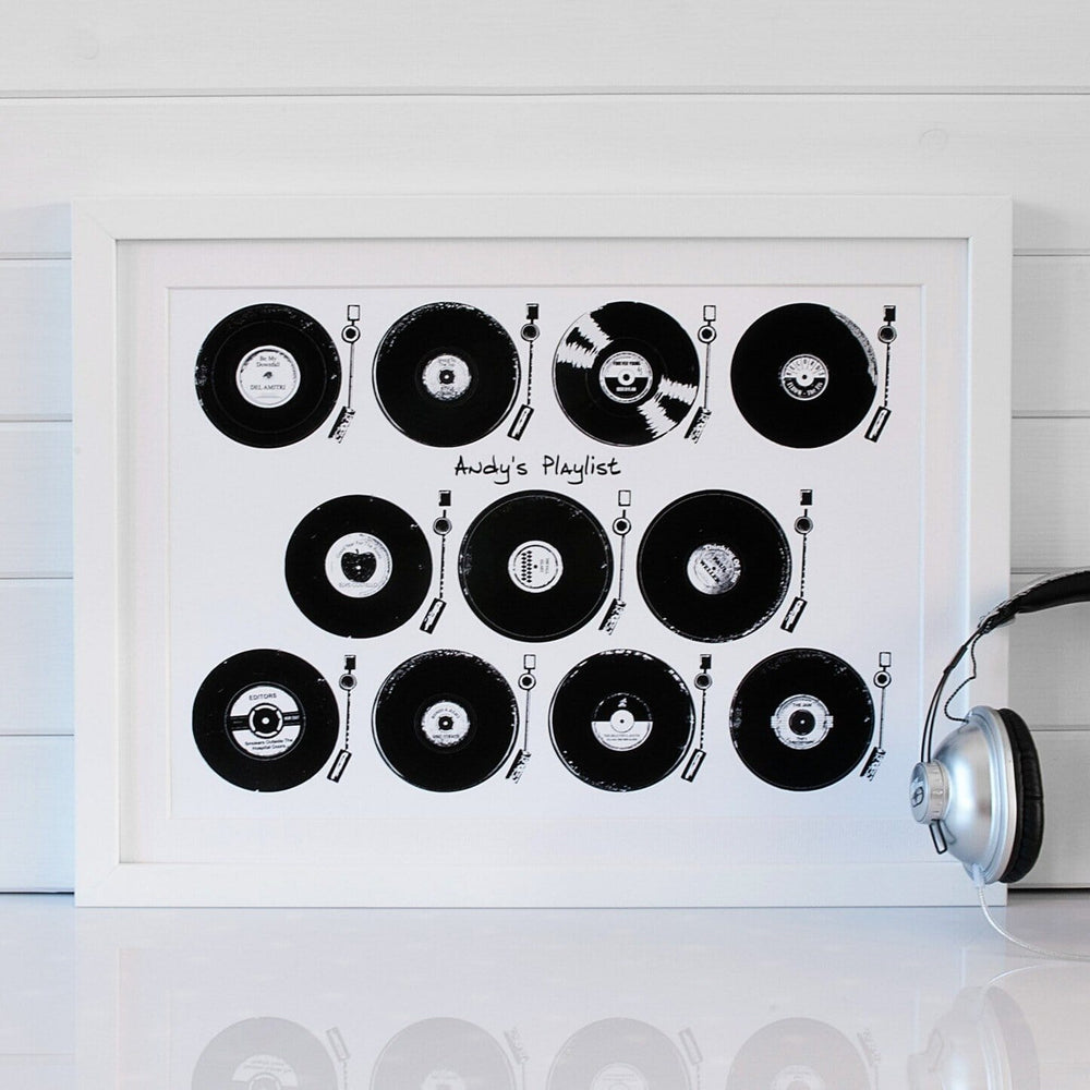 A framed print featuring a collection of vintage vinyl records playing on record players. The title "Andy's Playlist" is displayed at the bottom. A pair of headphones rests on a table nearby.