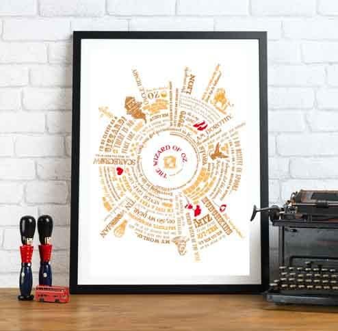 Framed The Wizard of Oz typography art print in gold and red, displayed on a wooden surface against a white brick wall, with a vintage typewriter and decorative objects nearby.
