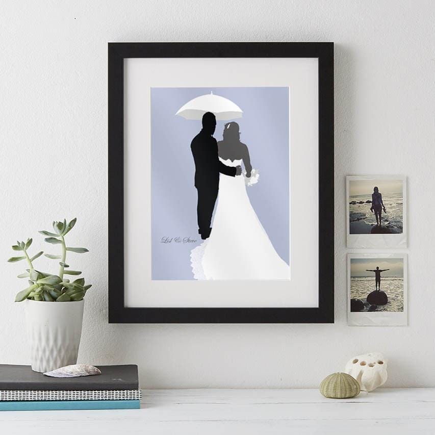 A wedding silhouette portrait in a black frame. The bride and groom are standing under a white umbrella on a pastel blue background. The words "Sealed Our Story" are written below.