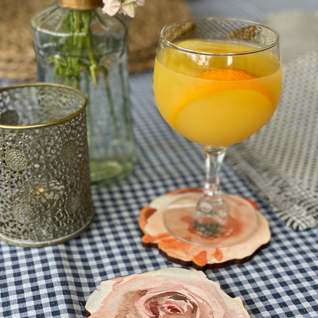 Wooden coasters featuring a watercolor floral design, with a glass of a refreshing cocktail and flowers in the background.