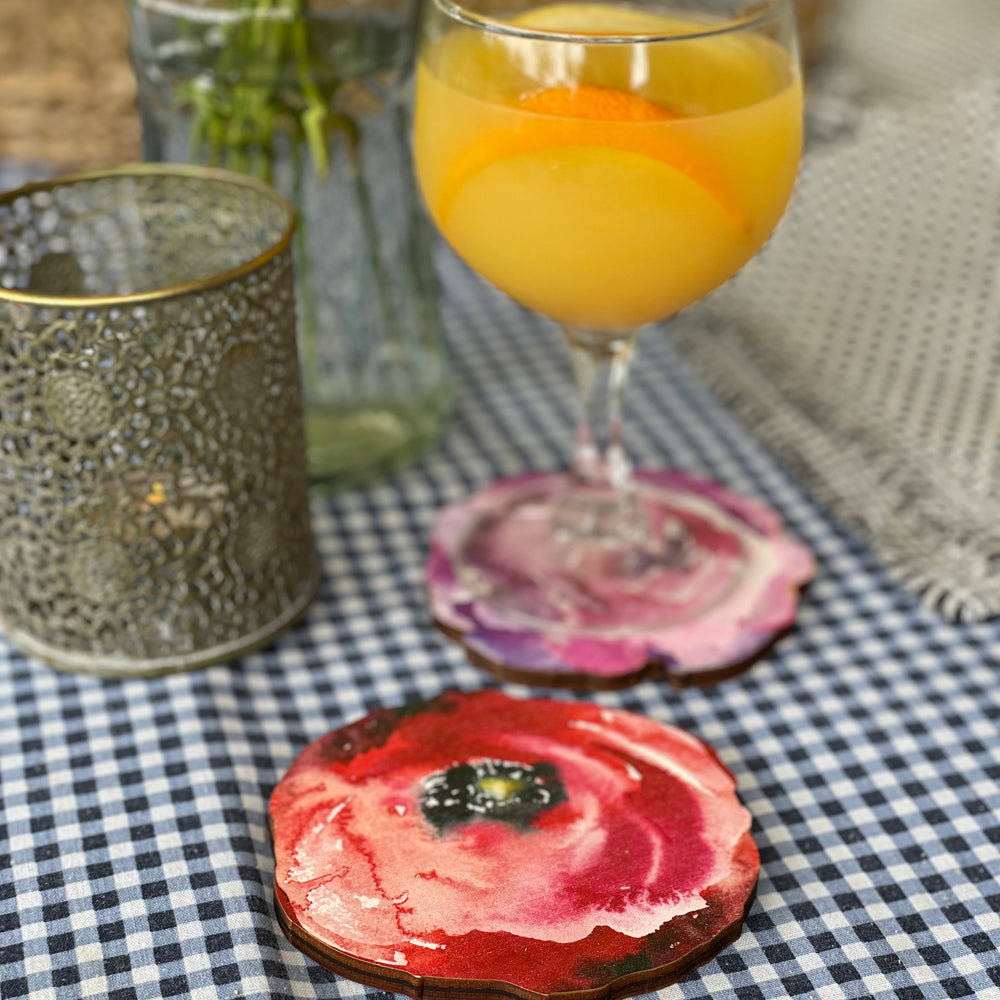 A delightful scene featuring a refreshing cocktail in a glass, resting on a vibrant red poppy flower-patterned wooden coaster. 